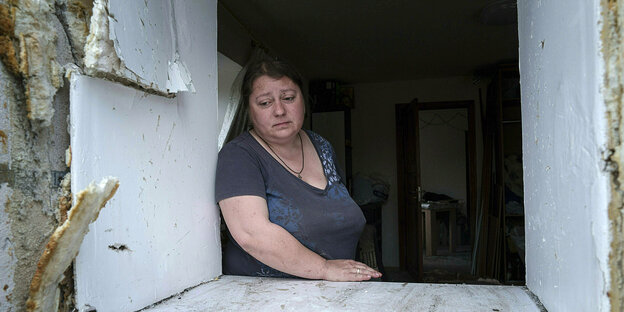 Eine Frau schaut traurig durch eine Wandöffnung, in der sich einmal ein Fenster befand