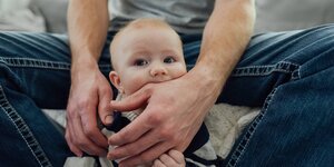 Ein Säugling spielt mit der Hand einer männlichen Bezugsperon