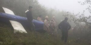 Männer stehen im Nebel vor abgestürztem Hubschrauber