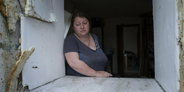 Eine Frau schaut aus dem Fenster eines zerstörten Gebäudes