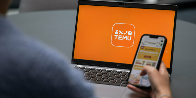 Ein Laptop mit orangenem Bildschirm und Firmenlogo "Temu", davor Smartphone in einer Hand, geöffnet ist eine Shopping-App