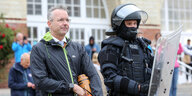 Nikolas Häckel steht während der freiwilligen Räumung des Punk-Protestcamps in Westerland auf Sylt neben einem Polizisten in Schutzausrüstung.