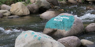 Mit Protest-Botschaften angemalte Steine liegen in einem Fluss.