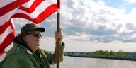 Ein Mann steht an einem Fluss und hält eine amerikanische Flagge.