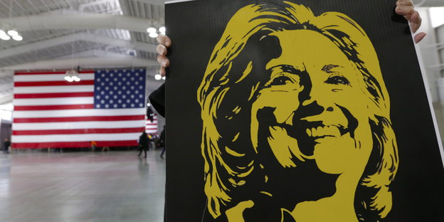 Plakat mit einem aufgesprühten Konterfei Hillary Clintons, daneben die US-Flagge