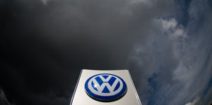 Das Logo des VW-Konzerns ist vor dunklen Wolken am Himmel zu sehen.