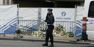 Ein Polizist steht vor einer Absperrung am Anschlagstatort in der Brüsseler U-Bahnstation. Trauerkränze liegen am Boden