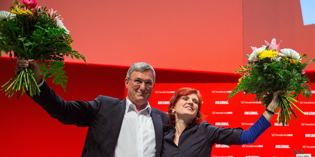 ein Mann und eine Frau mit jeweils einem großen Blumenstrauß in der Hand vor roten Hintergrund