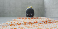 Auf einem orange gemusterten Stoff liegt ein großer schwarzer Babykopf als Skulptur