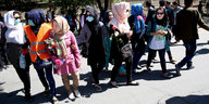 Frauen mit Kopftuch, teilweise mit Mundschutz, auf einer Straße bei Sonnenschein