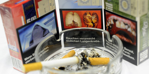 Drei Zigarettenschachteln mit Bildern von einer Raucherlunge, fauligen Zähnen und einer Leiche