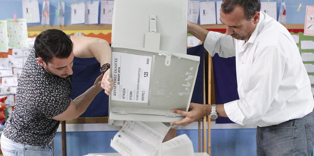 zwei Männer leeren eine Wahlurne aus