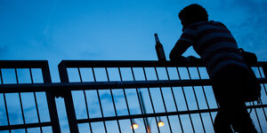 Die Silhouette eines Mannes mit Bierflasche auf einer Brücke.