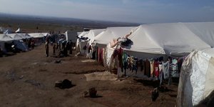 Zelte in einem Flüchtlingslager. Davor Menschen