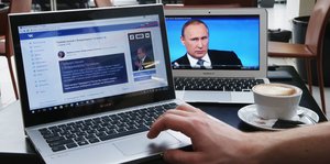 Zwei Laptops, auf dem Bildschirm des einen ist Putin zu sehen, auf dem anderen ist ein soziales Netzwerk geöffnet