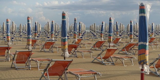 Leere Liegestühle und zusammengeklappte Sonnenschirme an einem Strand