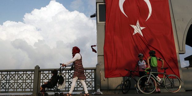 Eine Frau schiebt einen Kinderwagen über die Galata-Brücke in Istanbul, die mit einer riesigen Türkei-Fahne geschmückt ist.
