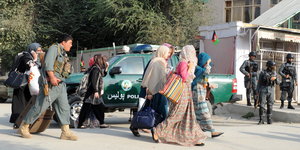 Männer mit Waffen begleiten Frauen vor dem Tor eines Gebäudes