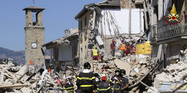 Feuerwehrleute in einer zerstörten Stadt, weiter hinten ein Kirchturm