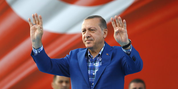 Erdogan mit zum Gruß erhobenen Händen vor einer großen Türkei-Flagge