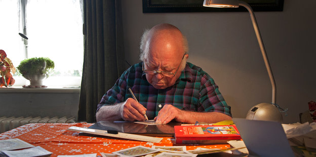 Ein älterer Herr malt an einem Tisch