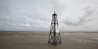 Ein gefakter Bohnturm steht am Strand, dahinter das Meer