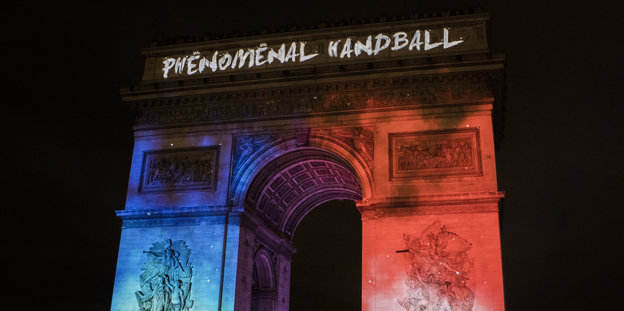 Der Arc de Triomphe in Paris bei Nacht. Er wird beleuchtet mit den fraanzösischen Worten "Phenomenal Handball"