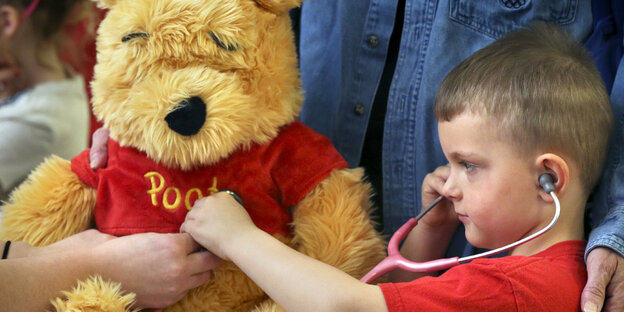 Ein kleiner Junge hört mit einem Stethoskop einen Teddybär ab.