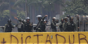 Schwer bewaffnete Polizisten stehen hinter einem gelben Banner, auf dem Dictadura steht