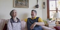 Ein Ehepaar sitzt lachend auf einem Sofa im Wohnzimmer