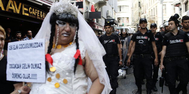 ein LGBTI-Community-Mitglied im Hochzeitskleid und mit Protestschild vor einer Reihe von Polizisten