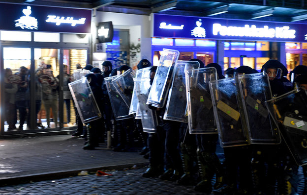 Polizisten in einer Straße, Menschen suchen hinter den Scheiben eines Restaurants Schutz