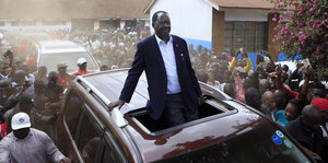 Raila Odinga fährt stehend in einem Auto durch eine Menge von Anhängern.