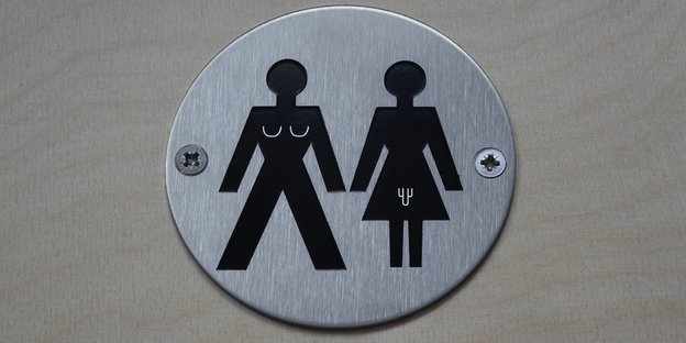 Auf einer Plakette sind Symbole von einem Mann mit Brüsten und einer Frau mit Penis Auf einer Plakette sind Symbole von einem Mann mit Brüsten und einer Frau mit Penis