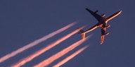 Im Licht der untergehenden Sonne zieht ein Flugzeug seine Kondensstreifen über den Himmel in Frankfurt am Main
