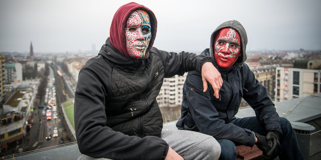 Zwei Männer sitzen auf dem Dach eines Hochhauses - mit Masken vor dem Gesicht Zwei Männer sitzen auf dem Dach eines Hochhauses - mit Masken vor dem Gesicht