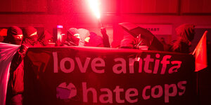Schwarz gekleidete und vermummte Demonstranten tragen ein Transparent mit der Aufschrift "love antifa, hate cops".