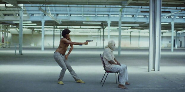 Szene aus dem Musikvideo, in dem Childish Gambino seine Waffen auf einen Mann richtet. Dieser sitzt mit Tuch über dem Kopf auf einem Stuhl.