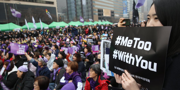 Eine Frau hält ein Schild, auf dem „#MeToo" und „#WithYou“ stehen