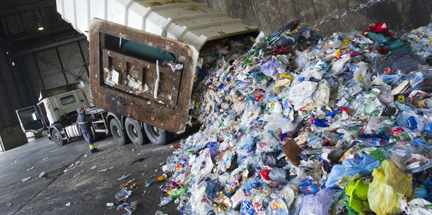Ein LKW kippt einen Haufen Plastikmüll in einer Halle auf den Boden