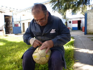 Ein Mann sitzt in einem Innenhof und näht an einem Ball Ein Mann sitzt in einem Innenhof und näht an einem Ball