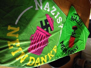 Zwei grüne Flaggen mit dem Aufdruck "Nazis - Nein Danke" und einem hakenkreuz, das in einer Mülltonne verschwindet