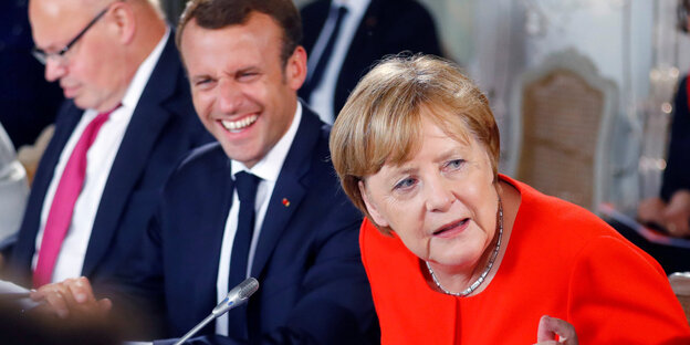 Die deutsche Bundeskanzlerin Angela Merkel wendet sich vom französischen Präsidenten Emmanuel Macron ab, der im Hintergrund lächelt