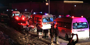 Mehrere Krankenwagen mit Alarmlicht, daneben stehen Personen