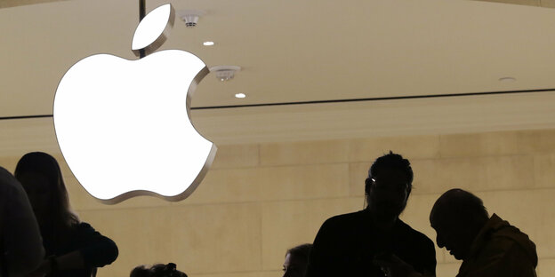Ein Apple-Logo hängt über den Silhouetten mehrerer Menschen Ein Apple-Logo hängt über den Silhouetten mehrerer Menschen