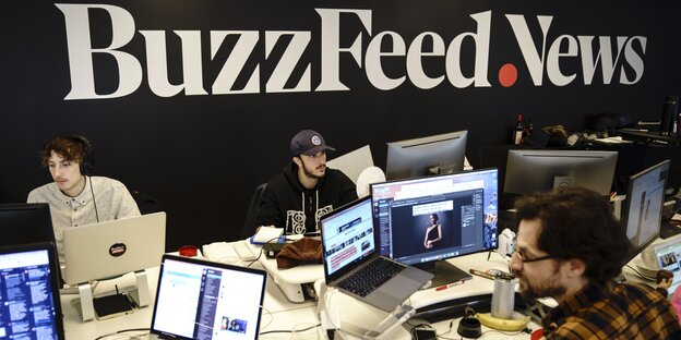 In einem Raum stehen zahreiche Computer, an denen Menschen arbeiten. An der Wand ist der große Schriftzug "BuzzFeed.News" zu lesen