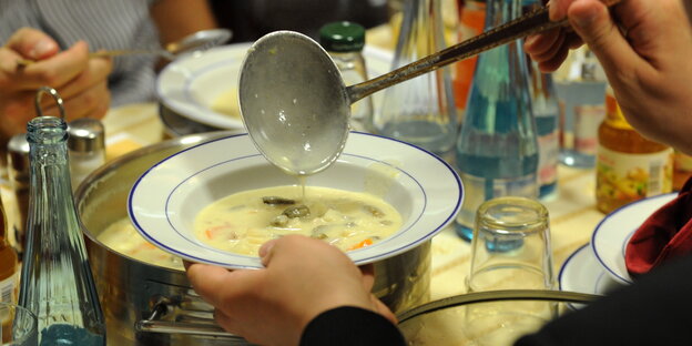 auf einem voll gedeckten Tisch schöpft jemand Suppe in einen Teller
