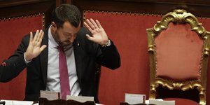Salvini sitzt im römischen Senat und hält die Handflächen von sich weg, als würde er schuld zurückweisen