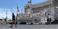 Passanten gehen vor dem Denkmal für König Vittorio Emanuele II. in Rom über Kopfsteinpflaster.