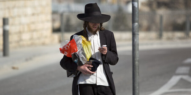 Junger Mann in orthodoxer jüdischer Kleidung blickt ins Smartphone